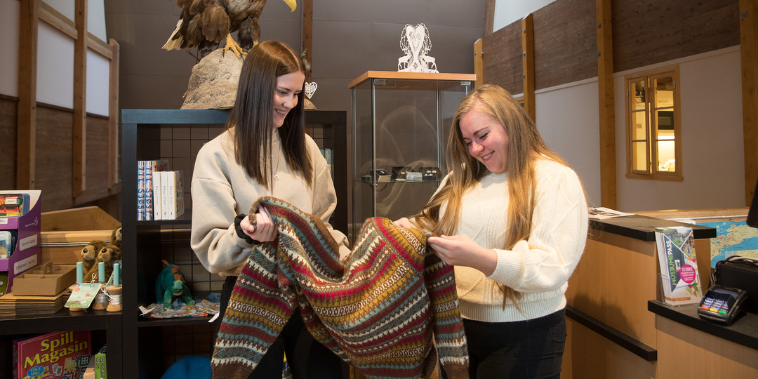 To kvinner studerer ei ulljakke i museumsbutikken.