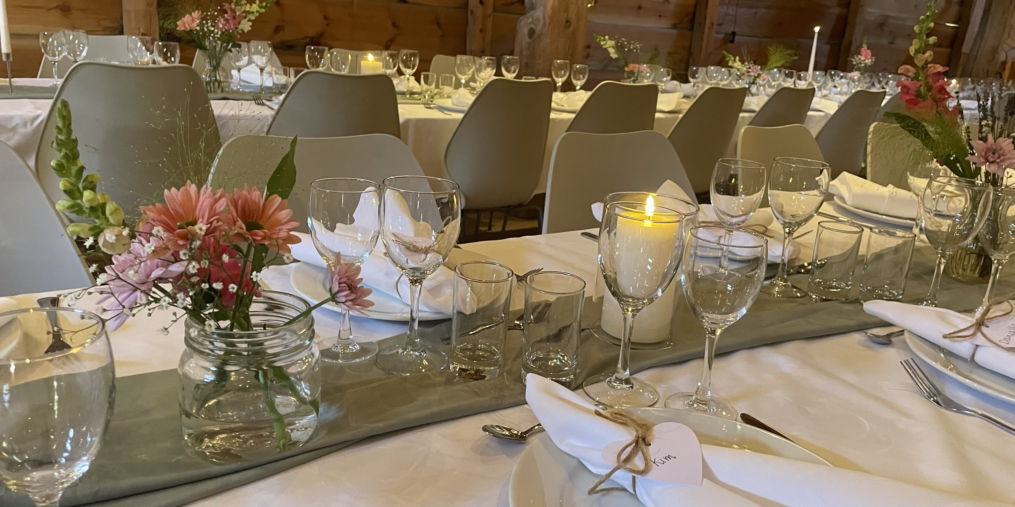 Utsnitt av odekorerte langbord til bryllaup. Borda er pynta med kvite dukar, stearinlys, serviettar med namnelappar og blomar.